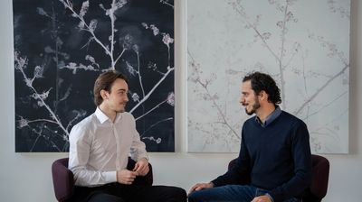 André Semadeni und Michael Naegeli sitzen während dem Interview vor zwei hängenden Bildern mit feinen Blumen.